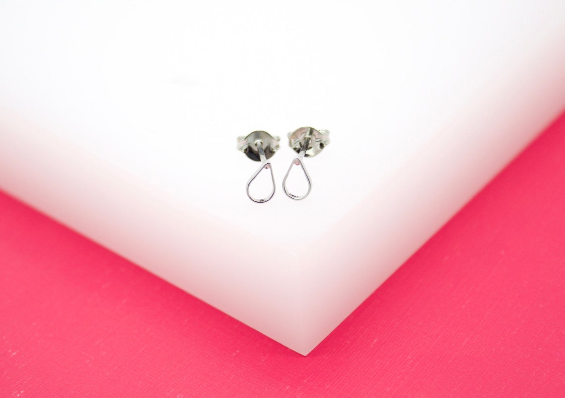 A pair of delicate silver teardrop stud earrings rests neatly on a clean white display surface.