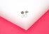 A pair of delicate silver teardrop stud earrings rests neatly on a clean white display surface.