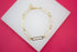 A stylish gold paperclip chain bracelet rests on a white display surface against a vibrant pink background.