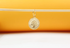 A delicate gold coin pendant hangs from a wooden stick against a warm yellow and white background.