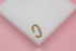 A gold beaded ear cuff rests on a white display block against a soft pink background.