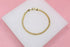 A delicate gold mesh chain bracelet rests on a white display stand against a soft pink background.