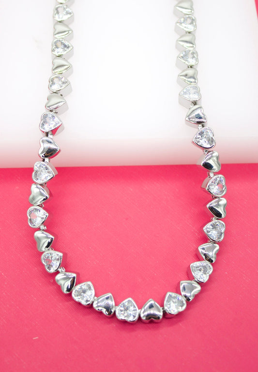 A dazzling silver heart-shaped tennis necklace rests against a vibrant pink backdrop.