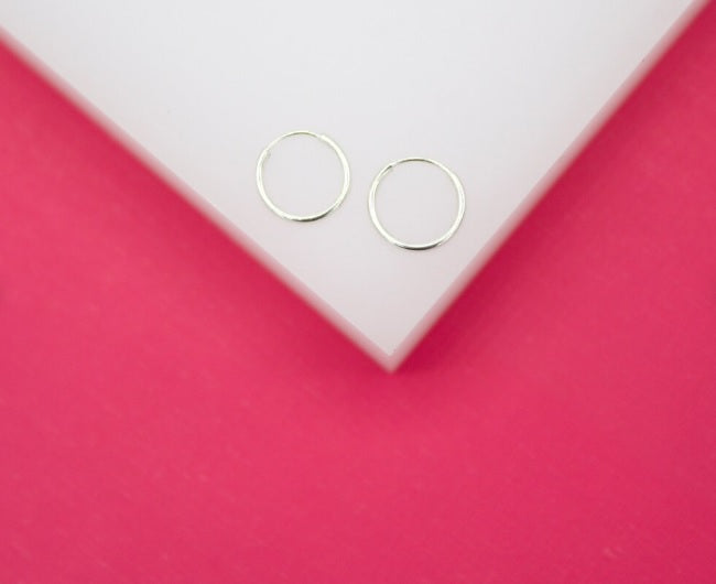 A pair of thin silver hoop earrings rests on a white block against a vibrant pink background.