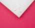 A pair of thin silver hoop earrings rests on a white block against a vibrant pink background.