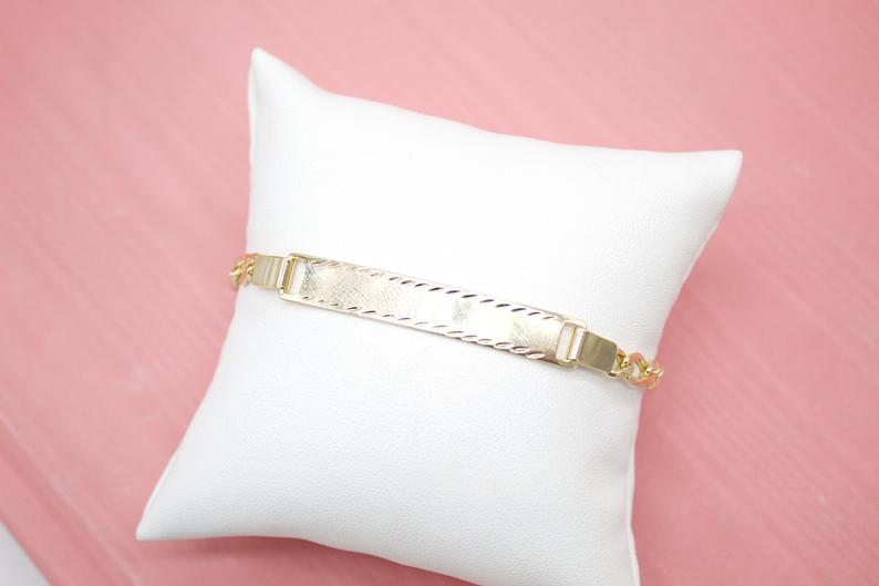 A shiny gold ID bracelet rests elegantly on a plush white display pillow.