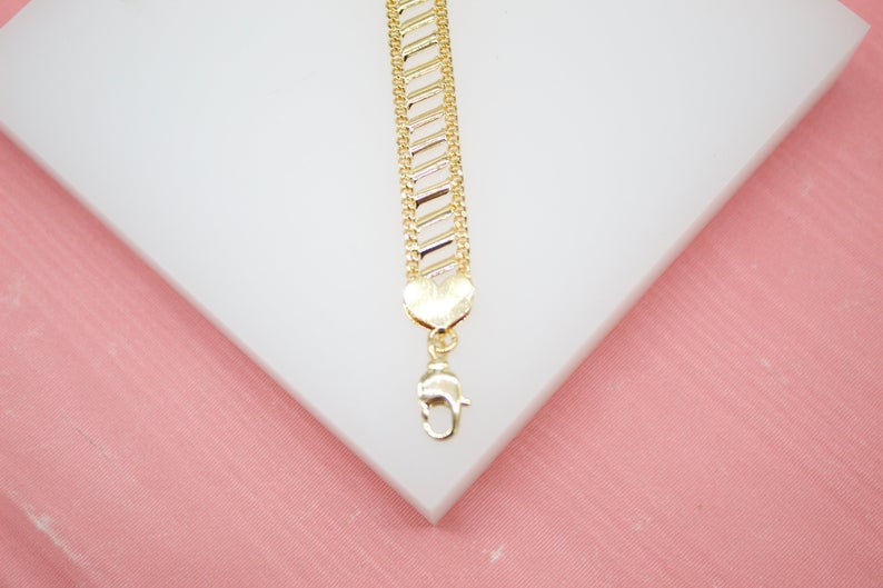 A textured gold bracelet featuring a heart-shaped charm and clasp rests on a white display surface.