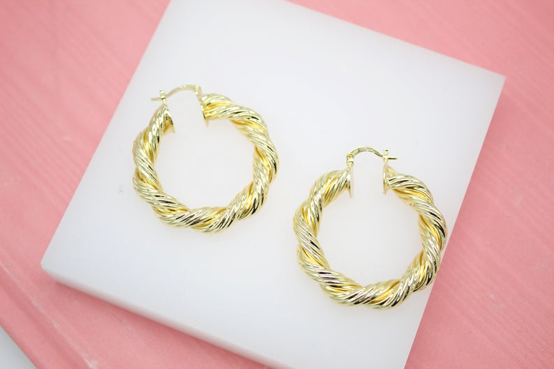 A pair of elegant twisted gold hoop earrings rests on a white display pad.