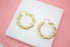 A pair of elegant twisted gold hoop earrings rests on a white display pad.