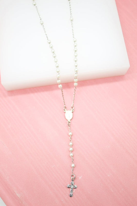 A delicate white pearl rosary necklace with a silver crucifix rests on a pink surface.