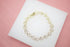 A delicate gold heart link bracelet rests on a white display surface against a pink background.