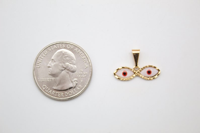 A gold double evil eye pendant rests next to a US quarter for size comparison.