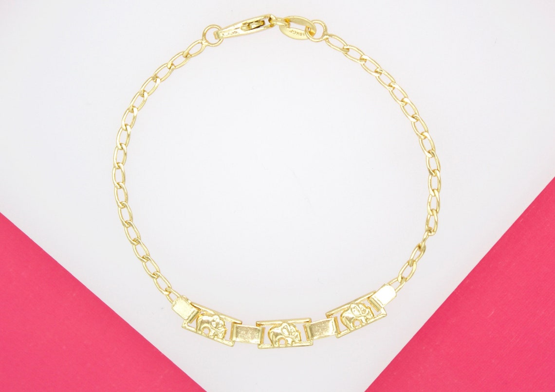 A gold link chain bracelet features three rectangular charms with embossed elephant designs against a pink and white background.