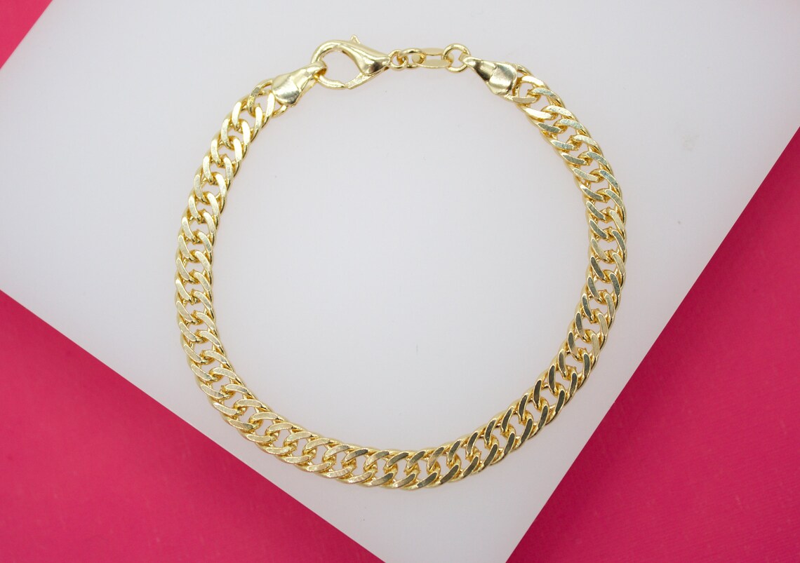 A gleaming gold cuban link chain bracelet rests on a white and pink surface, showcasing its secure lobster clasp.