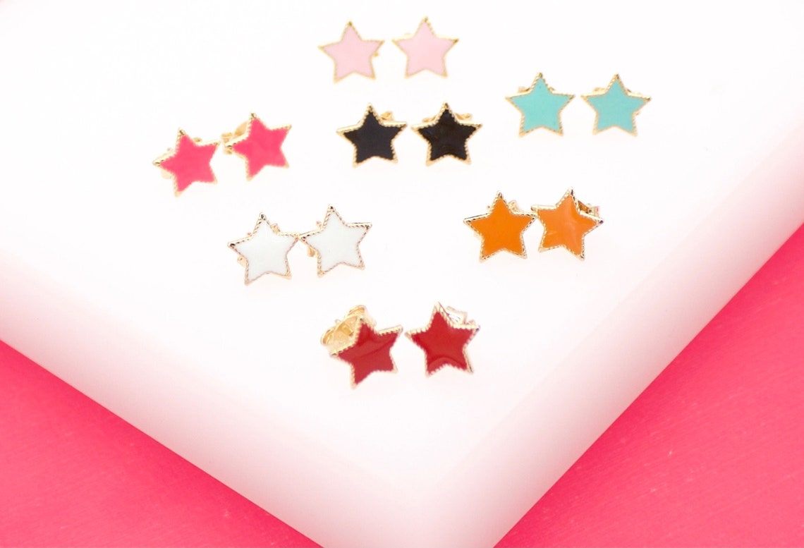 A collection of colorful enamel star-shaped stud earrings displays pairs in red, pink, black, white, orange, and blue on a white display surface.