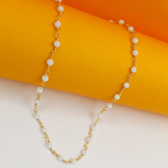 A delicate gold chain necklace adorned with small white beads drapes gracefully against a vibrant yellow and white background.