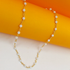 A delicate gold beaded necklace with white stones drapes against an orange and white background.