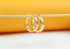 Two polished gold hoop earrings hang delicately from a thin horizontal stick against a warm yellow and white background.