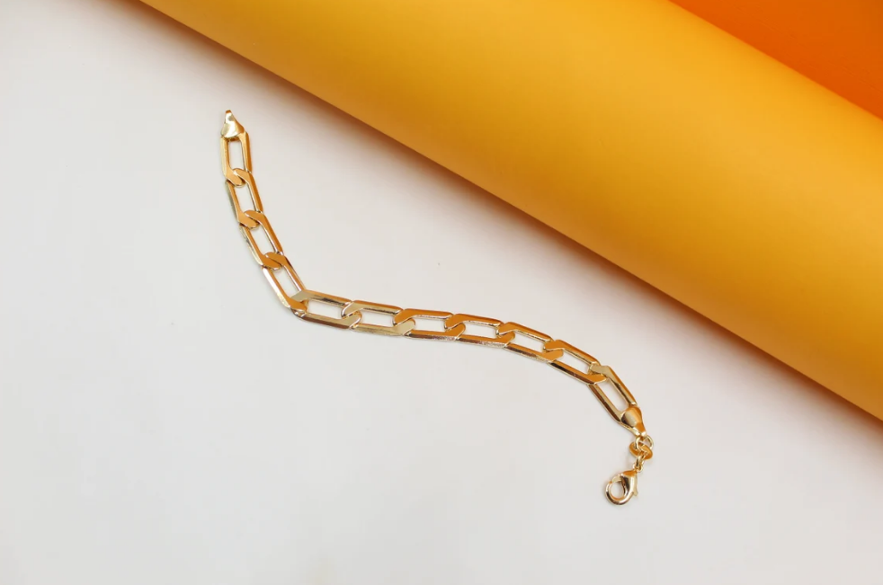 A sleek gold chain bracelet rests elegantly against a modern yellow and white background.