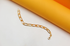 A sleek gold chain bracelet rests elegantly against a modern yellow and white background.
