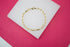 A delicate gold paperclip chain bracelet rests on a white display against a vibrant pink background.