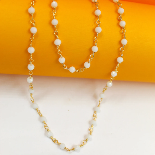 A delicate gold chain necklace featuring small white beaded stations drapes elegantly against a vibrant orange and white background.