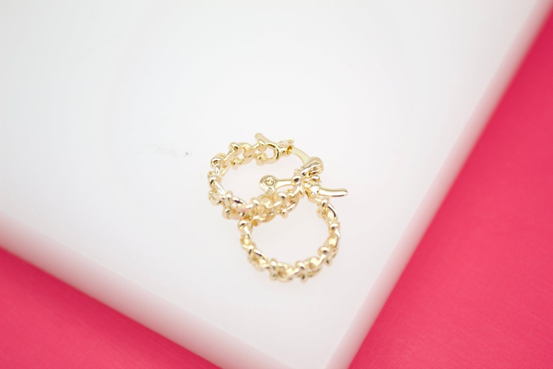 A pair of gold textured huggie hoop earrings rests on a white and pink surface.