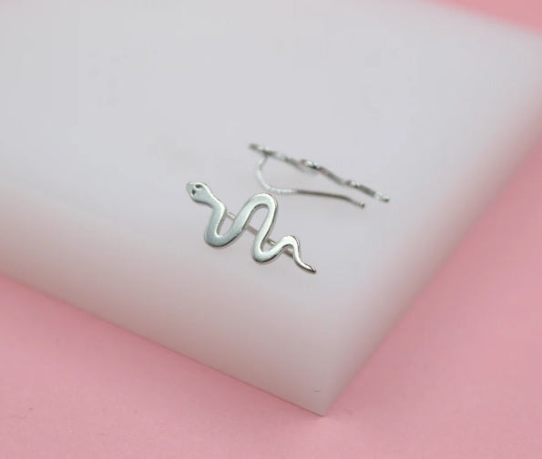 A sterling silver snake crawler earring rests on a white display block against a soft pink background.