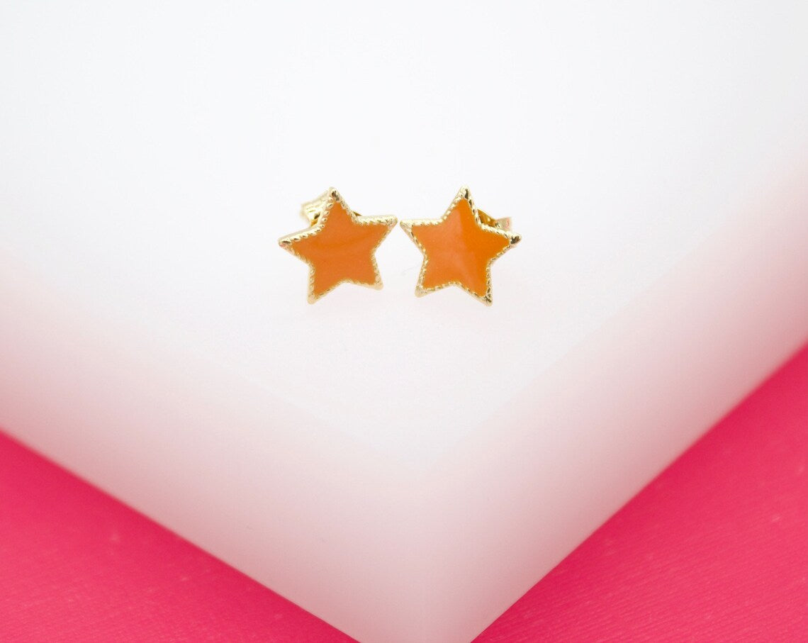 A pair of orange enamel star-shaped stud earrings rests on a white display surface against a pink background.