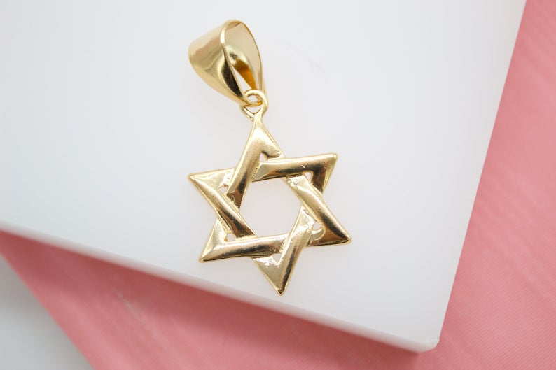 A polished gold Star of David pendant rests against a white display surface.
