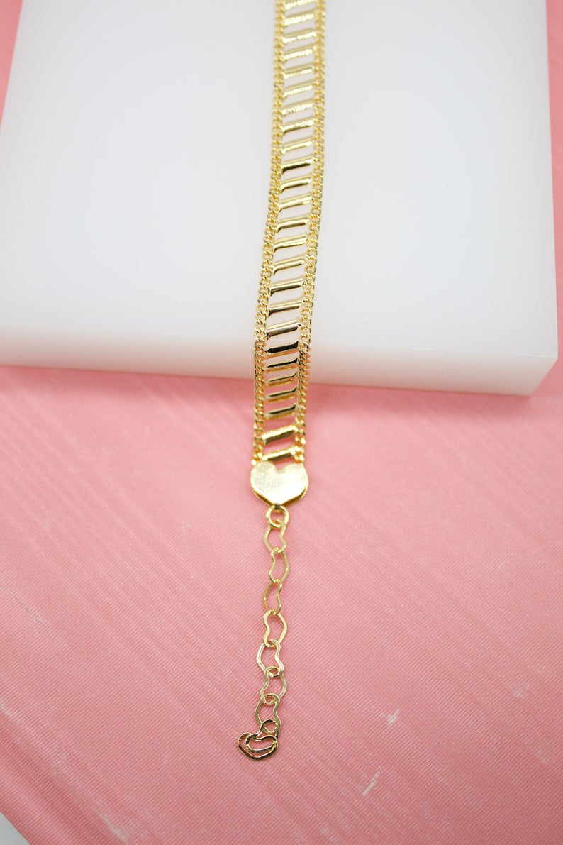 A gleaming gold-plated bracelet with a ladder-link design rests on a white and pink display surface, featuring an extension chain of interlocking hearts.