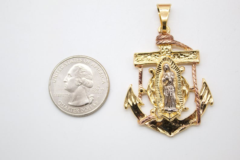 A two-tone gold Our Lady of Guadalupe anchor pendant rests beside a US quarter for scale.