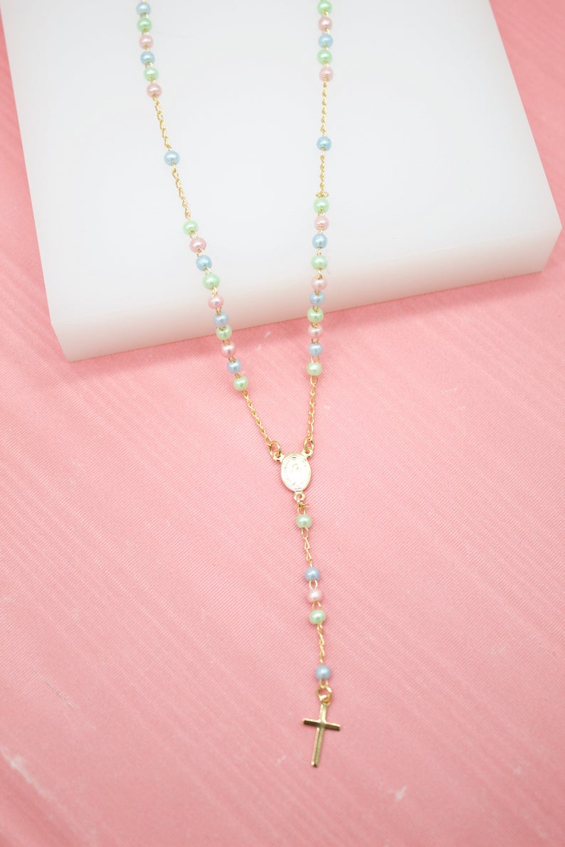 A delicate gold rosary necklace featuring pastel-colored pearl beads rests on a pink and white display surface.