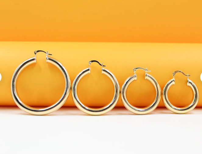 Four polished gold hoop earrings display a graduated range of sizes arranged in a row against a vibrant orange and white background.