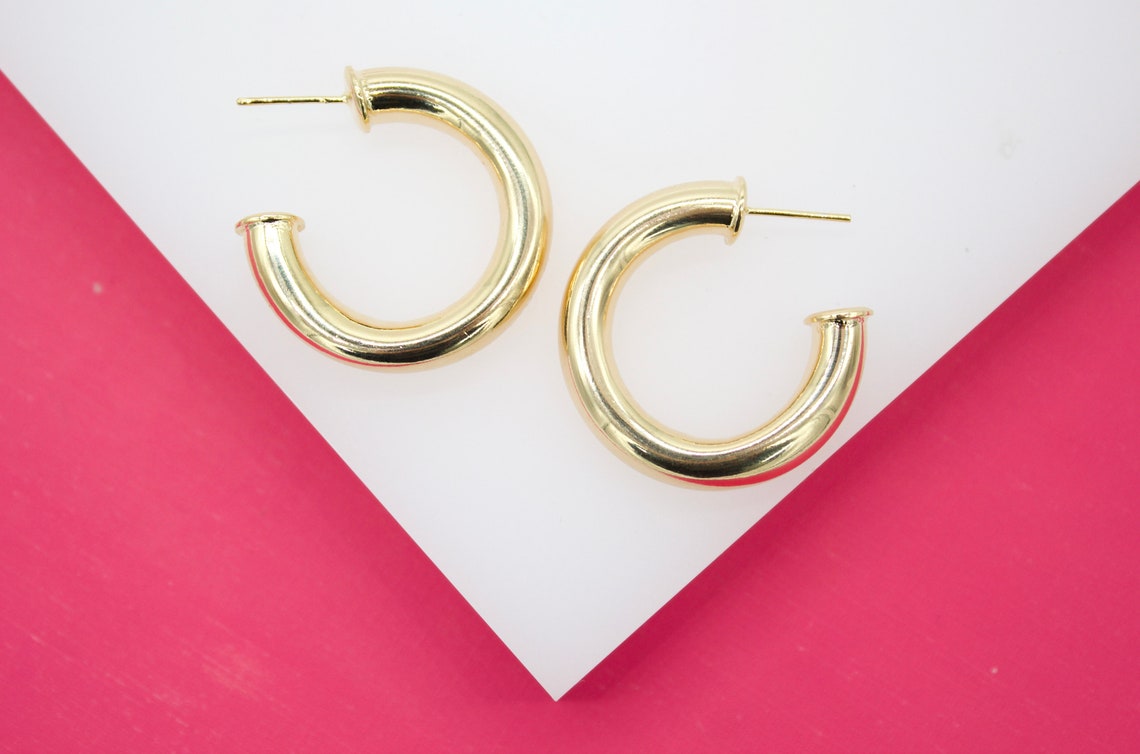 A pair of thick gold hoop earrings rests on a white and pink geometric display.