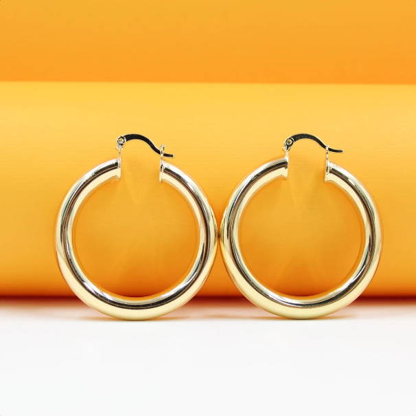 A pair of polished thick gold hoop earrings rests against a vibrant orange and white background.