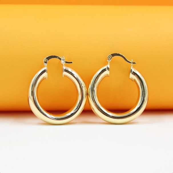 A pair of polished gold hoop earrings rests against a vibrant orange and white background.