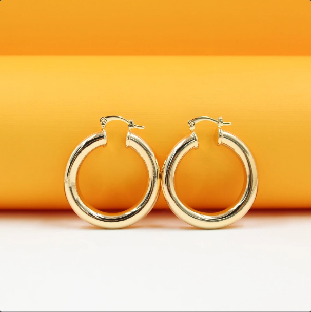 A pair of polished gold hoop earrings rests against a vibrant orange and white background.