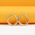 A pair of polished gold hoop earrings rests against a vibrant orange and white background.