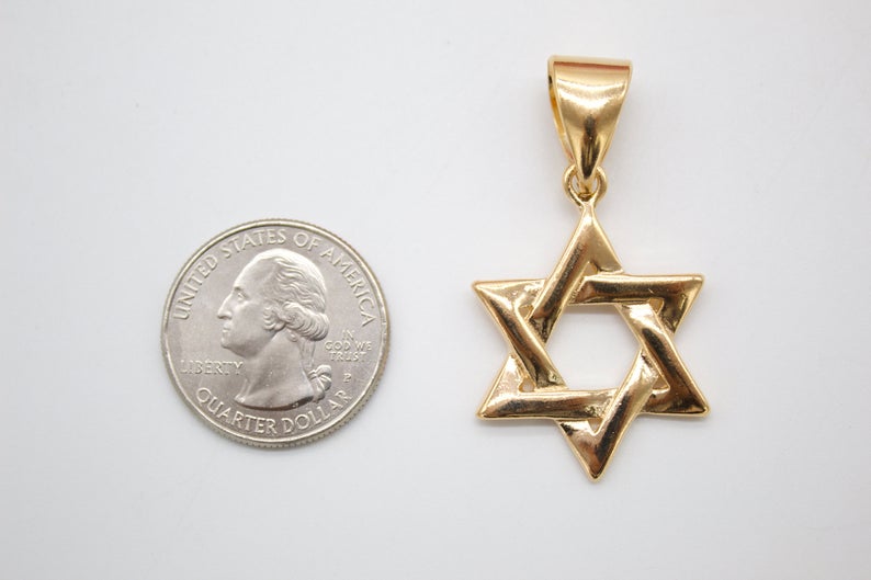 A polished yellow gold Star of David pendant rests next to a US quarter coin to display its actual size.
