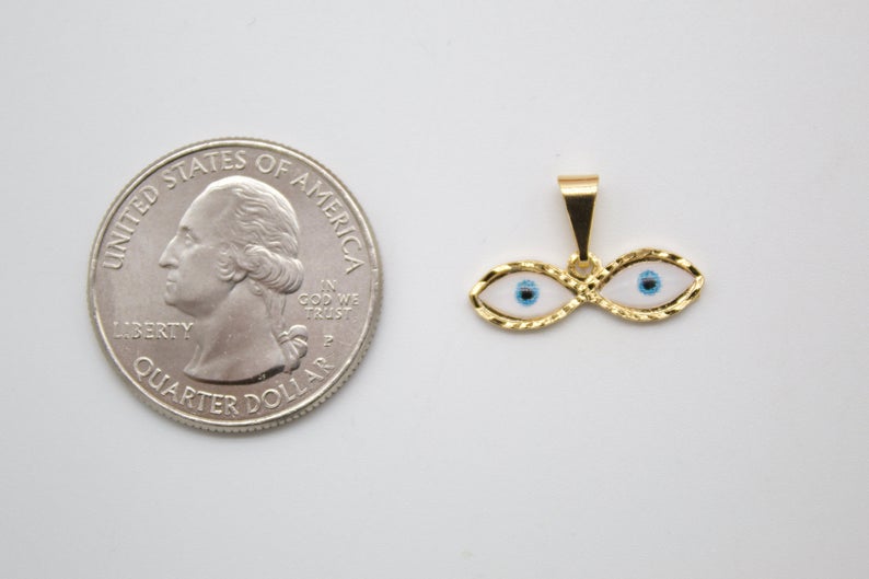 A gold evil eye pendant rests next to a US quarter coin to show its small size.