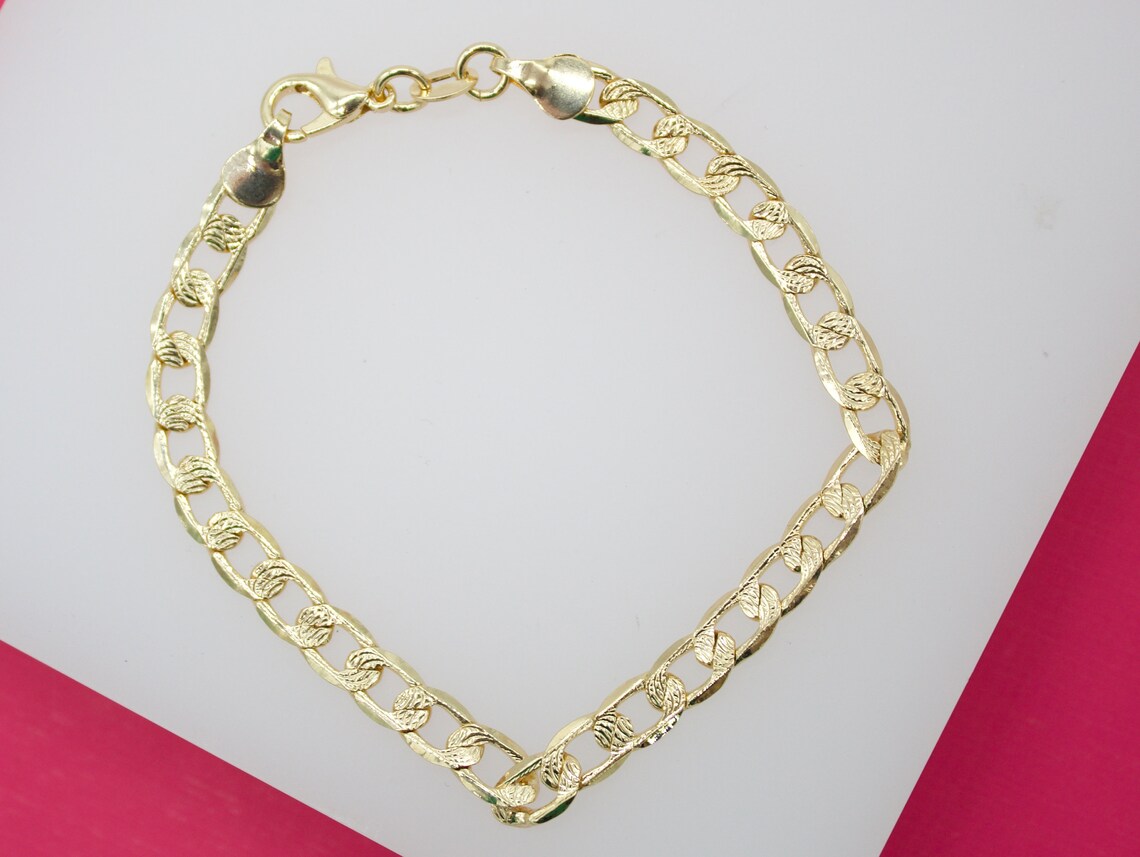 A gleaming gold link bracelet lies arranged in a gentle curve against a contrasting white and pink background.