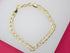 A gleaming gold link bracelet lies arranged in a gentle curve against a contrasting white and pink background.