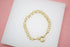 A gold-plated link bracelet rests on a white display surface against a pink background.