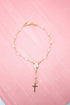 A delicate gold rosary bracelet with crystal beads rests against a vibrant pink background.