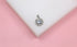 A sparkly silver halo diamond pendant rests on a white display against a soft pink background.