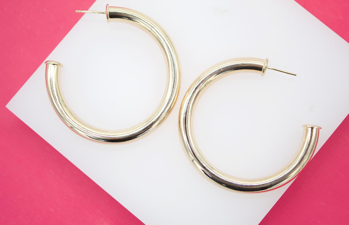 A pair of thick gold hoop earrings rests on a white display against a vibrant pink background.