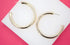 A pair of thick gold hoop earrings rests on a white display against a vibrant pink background.