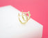 A pair of gold huggie hoop earrings with sparkling crystal accents rests on a white display surface against a vibrant pink background.