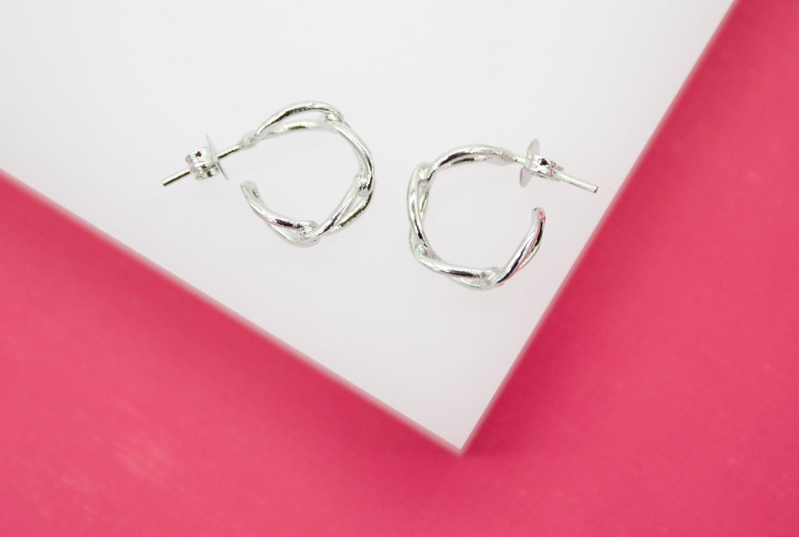 A pair of silver twisted hoop earrings rests on a white and pink display surface.